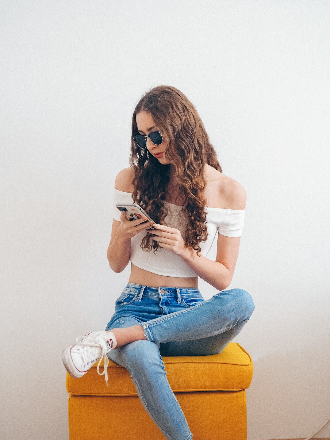 Smiling young woman with glasses holding a phone and reading news